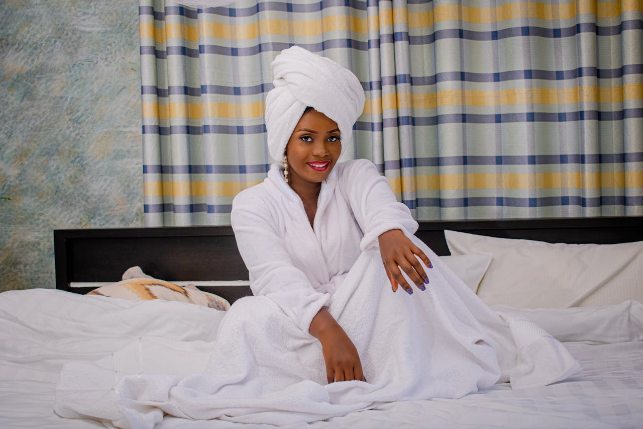 Smiling woman in bathrobe sitting on a bed in a hotel room, embodying relaxation and leisure.