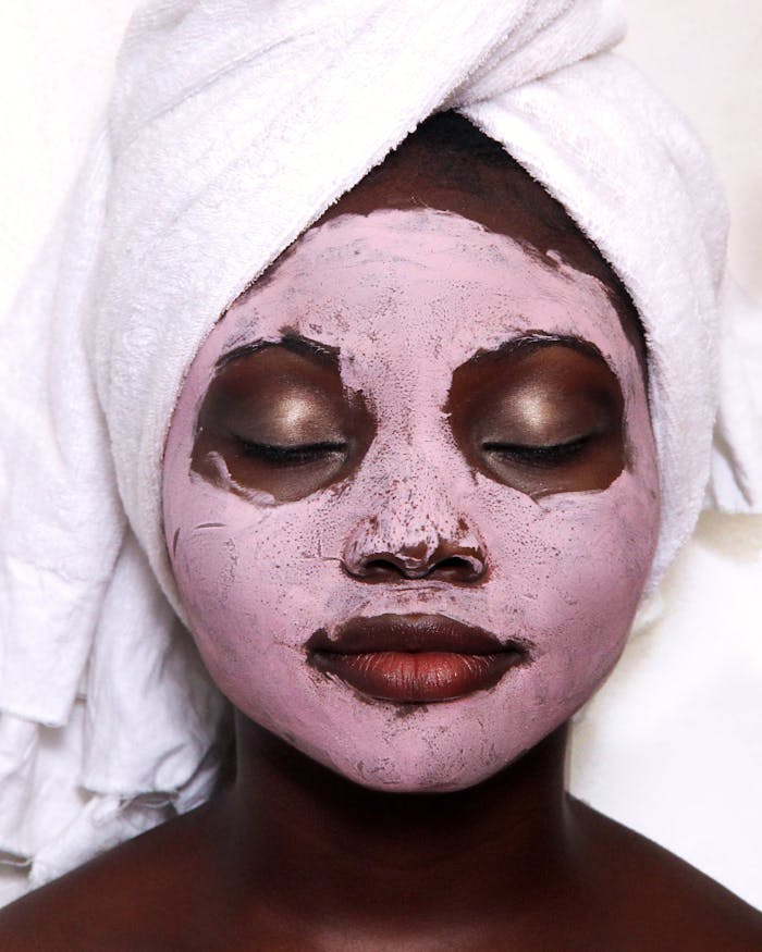 An African American woman with a clay facial mask and towel relaxes, symbolizing self-care.