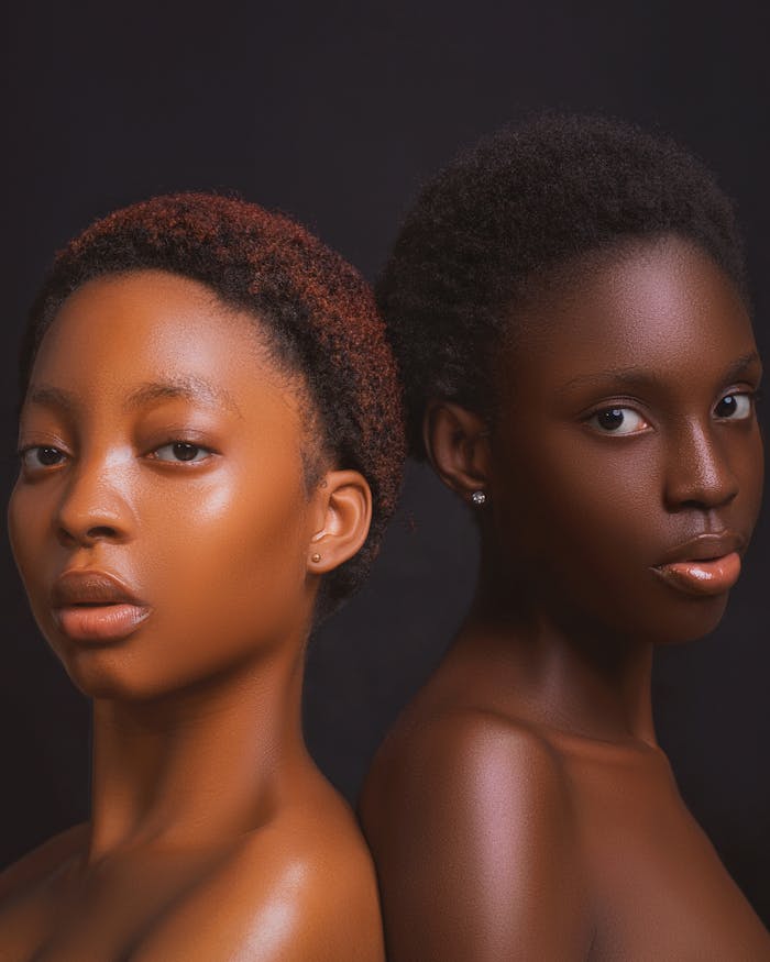 Studio portrait of two women with afro hair against a dark background showcasing beauty and sophistication.