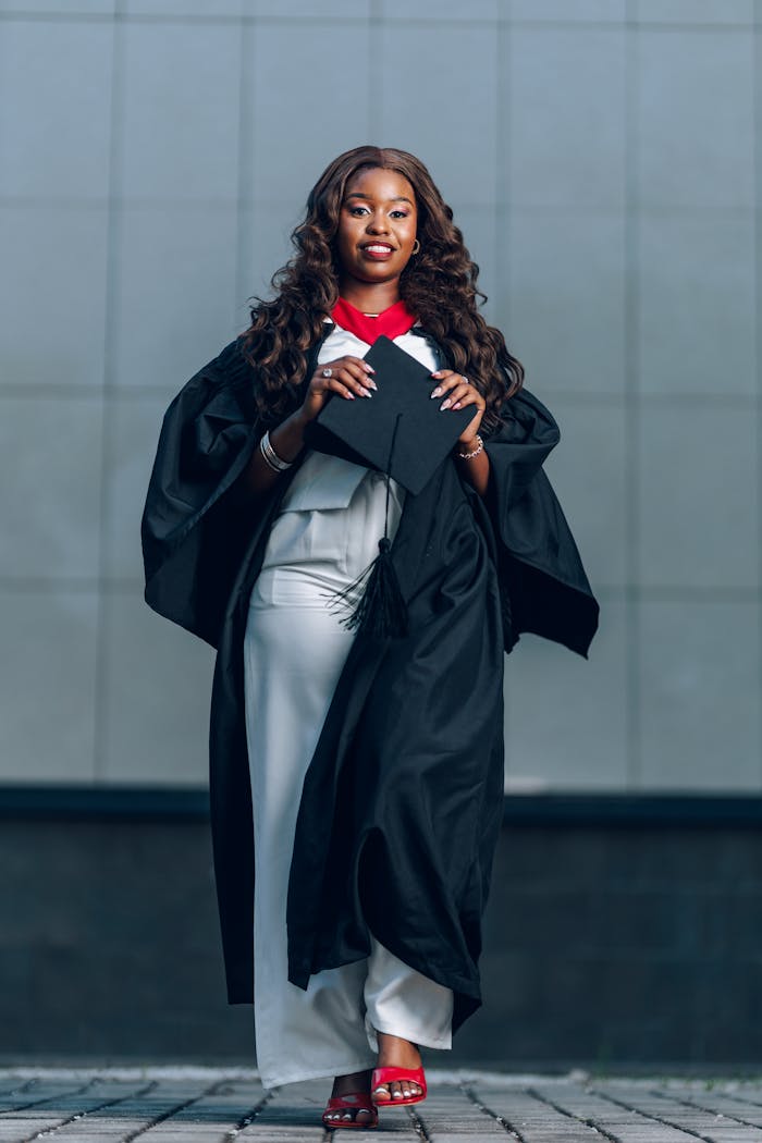A female graduate proudly holding her cap in a convocation gown, symbolizing achievement and success.